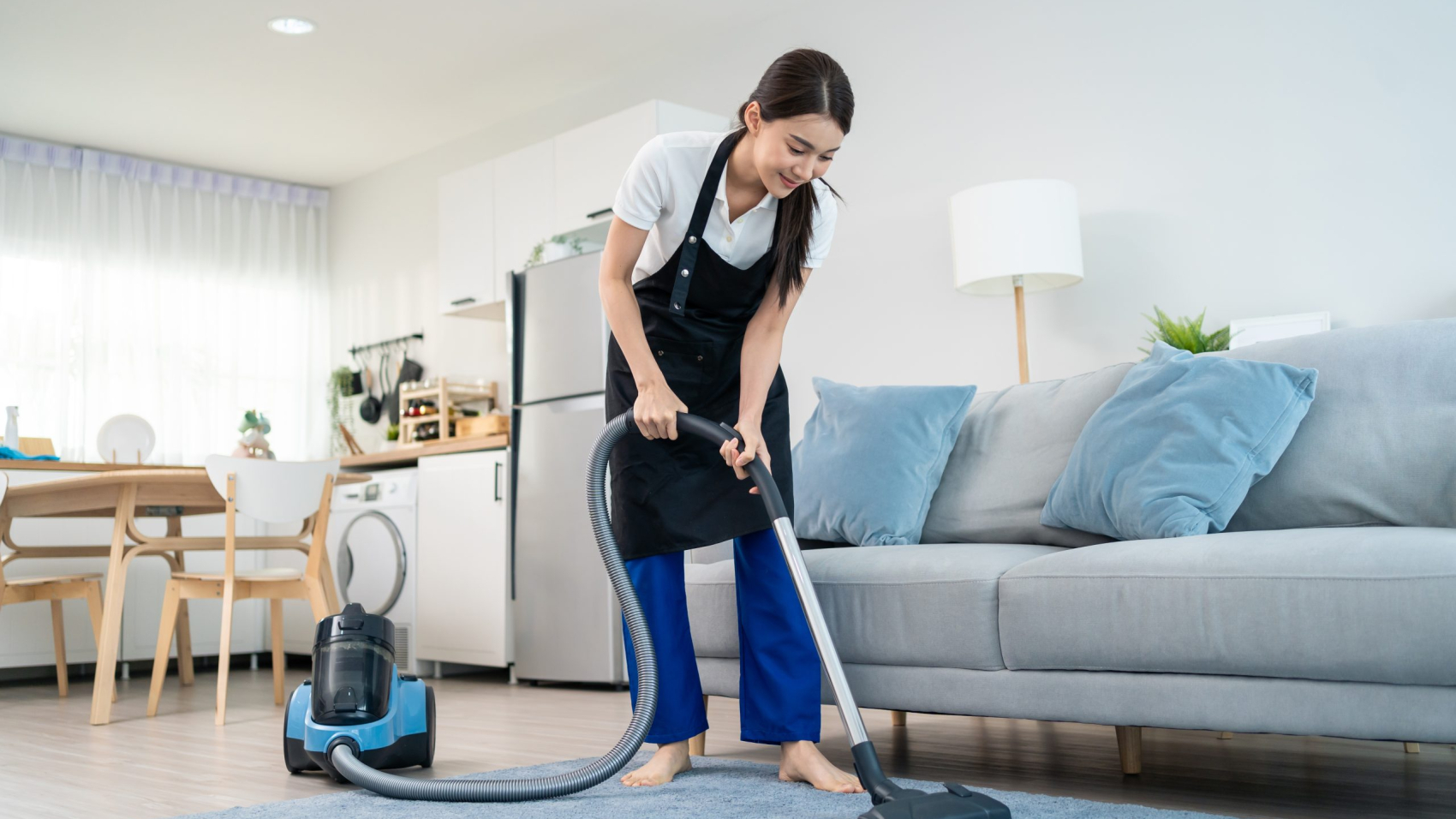 Asian cleaning service woman worker cleaning in living room at home. Beautiful young girl housekeeper cleaner wear apron and vacuuming messy dirty floor for housekeeping housework and chores in house.