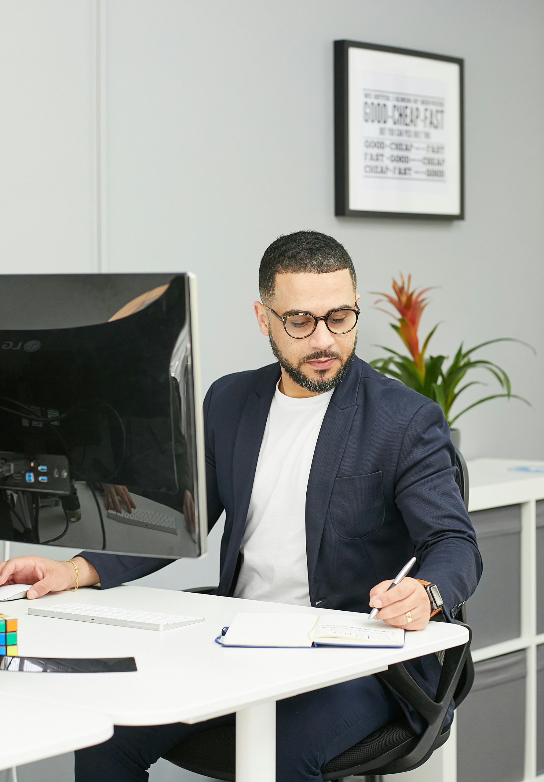 Consultant in glasses reviewing notes at a desk with dual monitors